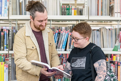 Two undergraduate students in a library looking at a book